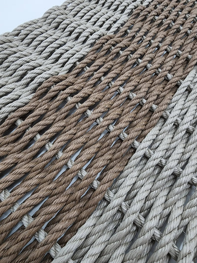 Handmade lobster rope mat in tan and brown colors, displayed on wooden floor