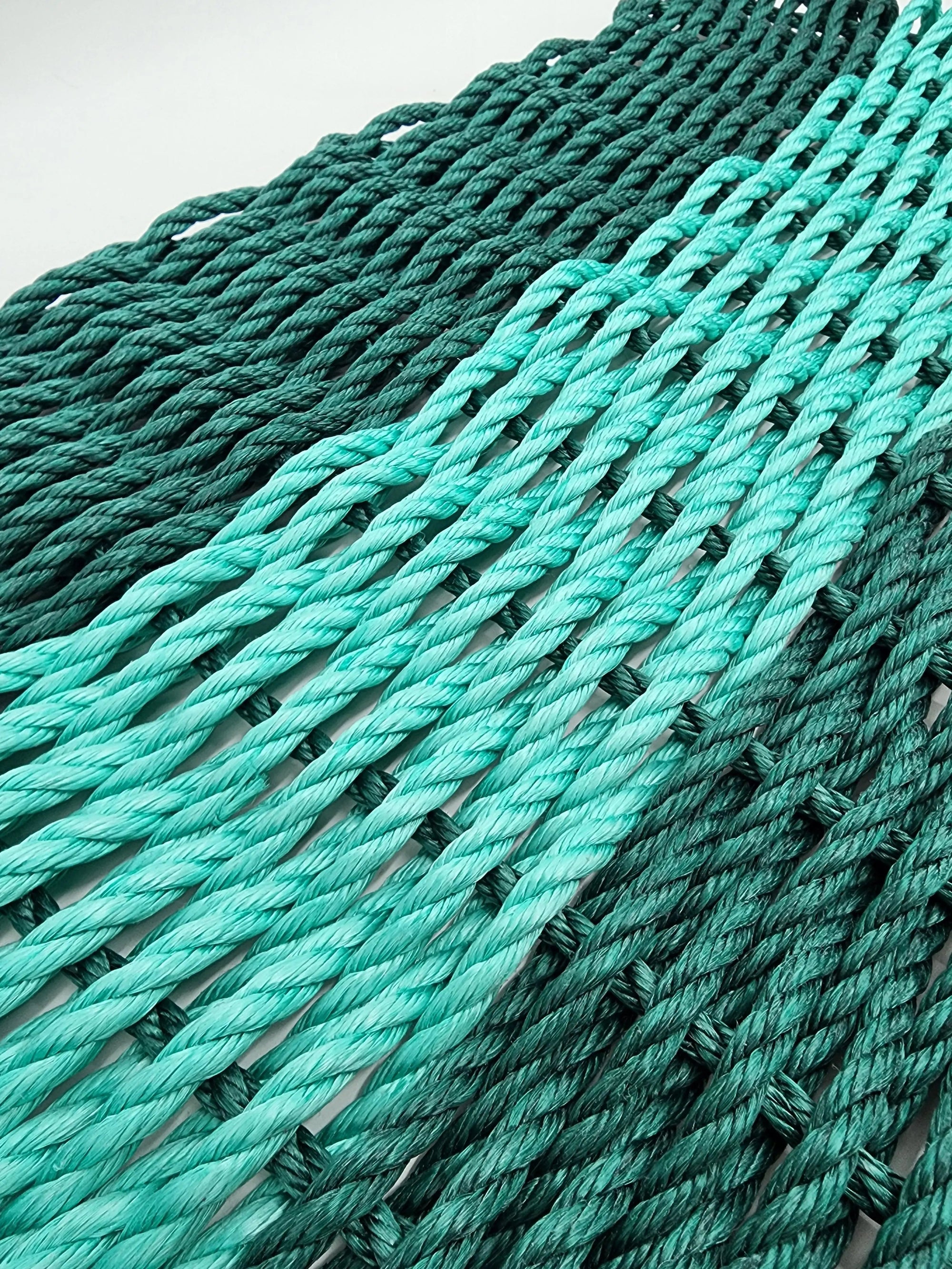 Hunter green and teal handmade lobster rope mat on wooden floor