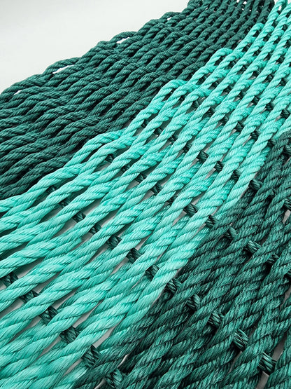 Hunter green and teal handmade lobster rope mat on wooden floor