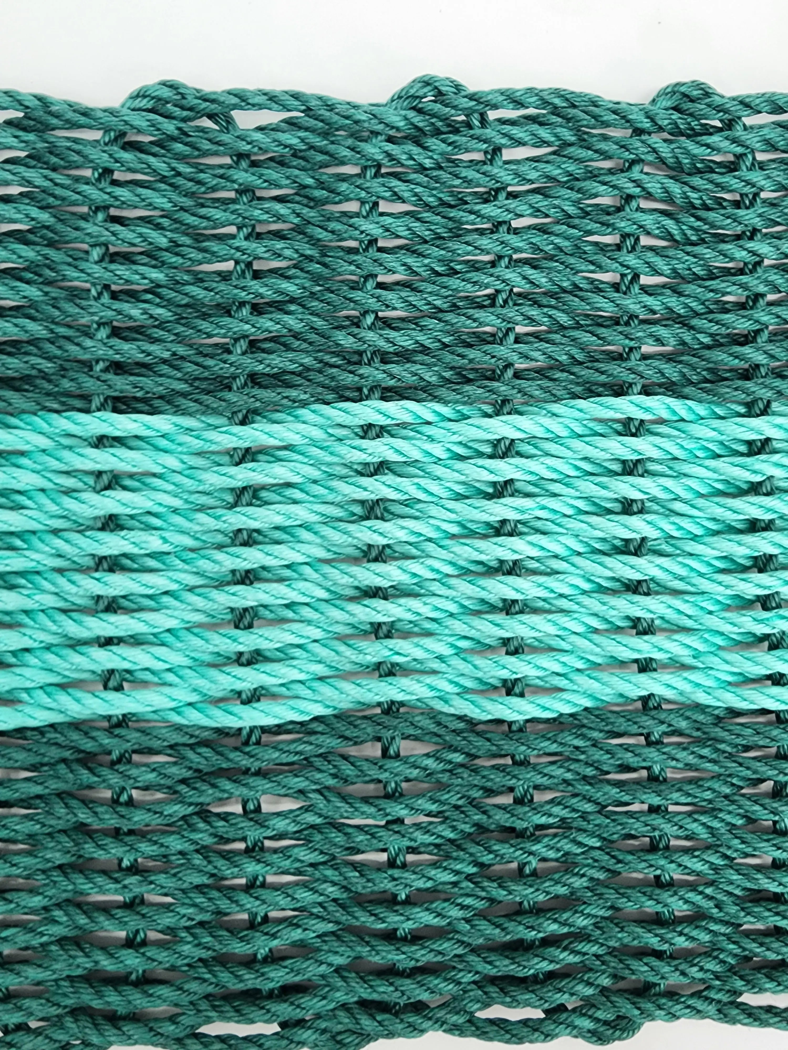 Hunter green and teal handmade lobster rope mat on wooden floor