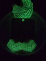 Macrame fringe earrings glowing bright green in the dark, displaying detailed twisted and fringed patterns with a triangular base card.