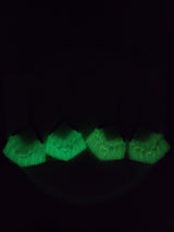 Four pairs of macrame earrings with glowing green fringes, arranged in a row against a dark background, highlighting their luminous texture and fringe details.