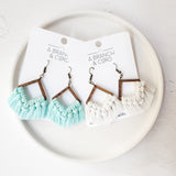 Blue glow-in-the-dark macrame fringe earrings hanging from a branch with soft natural background
