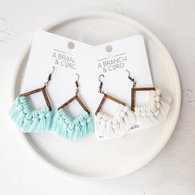 Blue glow-in-the-dark macrame fringe earrings hanging from a branch with soft natural background