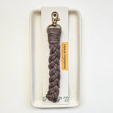 Taupe macrame braided key wristlet with antique brass lobster clasp, displayed on a rectangular off-white tray against a white background.
