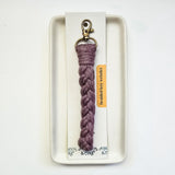 Mauve macrame braided key wristlet with brass lobster clasp displayed on a white rectangular tray and attached to a white card labeled 'braided key wristlet'