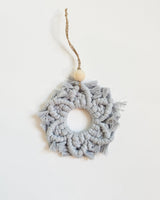 Gray macrame snowflake ornament with a circular center, knotted patterns, fringed edges, and a natural twine loop topped with a round wooden bead.