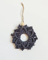 Gray macrame snowflake ornament with symmetrical knots and fringed edges, topped with a wooden bead and hanging from a twine loop.