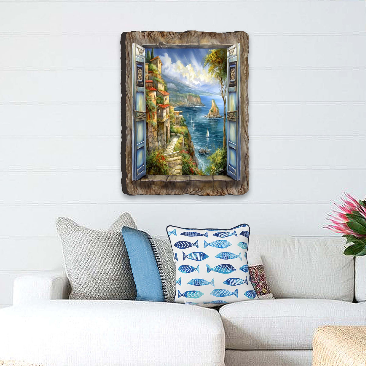 Seaside wall art showing an open blue window with shutters, overlooking a coastal village, sailboats, and cliffs under a partly cloudy sky.
