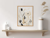 Framed floral abstract print with beige, black, and gray flowers and foliage, hanging above a light wood shelf with white ceramic vases and pampas grass.
