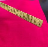 Close-up of a gold-toned utensil handle with a repeating geometric square pattern, resting diagonally on a bright pink fabric background.