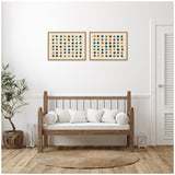 Two framed canvases each with a 7x7 grid of colorful dots in warm and cool tones, hanging side by side above a wooden bench with white cushions.