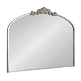 Arched wall mirror with antique silver frame and ornate carved floral crest centered at the top edge, reflective surface without beveling.