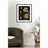 Framed floral artwork showing soft peach and pink flowers with green stems against a black background, hanging above a dark olive-green curved chair and next to a potted plant.