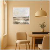 Neutral-toned abstract landscape painting with soft grays and browns, framed and hung on a beige wall above a wooden dining table with beige chairs and pendant light.