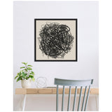 Black abstract scribble linework centered on beige background in a black square frame hanging above a light wood desk with a plant and metal sculpture, paired with a pale blue chair.