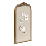 Tall arched pinboard with beige fabric surface and an ornate carved wooden frame featuring scroll and leaf motifs at the top center.
