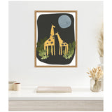 Framed canvas art print showing two yellow giraffes with brown spots under a large blue moon on a black background with green leaves at their feet.