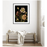 Framed floral art with soft peach and brown flowers and green stems on a deep black background, hanging above a light wood bench with a white throw and open book.