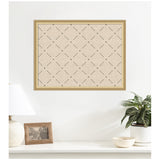 Beige fabric pinboard with a subtle green lattice pattern in a light wooden frame, mounted on a white wall above a white shelf with a lamp, photo, plant, and bowl.