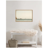 Seascape painting with a distant sailboat on calm Pacific waters, framed in light wood and hung above a white bench with a beige fur throw and gray bag below.