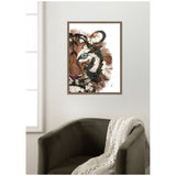 Framed canvas print of a tiger's head made from layered paper textures in brown, black, cream, and purple tones, hanging above a dark gray armchair with a cream knit throw.