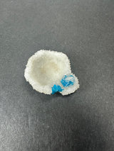 White crystalline stilbite formation with small bright blue cavansite crystals clustered on one edge, set against a plain dark gray background.