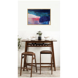 Abstract wall art in shades of blue, pink, and white above a dark wood bar table with two matching stools and minimal tableware, styled with a small plant.