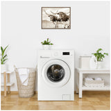 Sepia-toned framed canvas print of two Texas Longhorn cattle in a grassy pasture, hanging above a white front-loading washing machine in a minimalist laundry room.