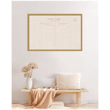 Large framed fabric pinboard designed like a vintage postcard with beige and brown tones, mounted on a light wall above a wooden bench with pale cushions and a vase of dried flowers.