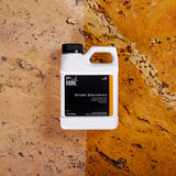 White plastic container of MORE Stone Enhancer with black label placed on a two-tone natural stone surface showing beige and golden orange colors with dark veins.