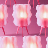 Three identical pink wavy lamps with ribbed translucent shades and tripod legs arranged against a solid pink background, glowing warmly from within.