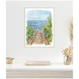 Watercolor painting of a wooden stairway descending to a blue ocean, framed with intricate white trim and surrounded by green foliage.