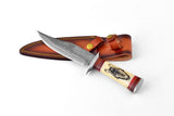 Knife with patterned Damascus steel blade and cream handle featuring a detailed black wolf head, shown with brown leather sheath with brass snaps.
