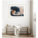 Abstract framed art with sweeping brushstrokes in deep blue, rust, and beige tones hanging above a wooden bench with an open book and draped fabric in a minimalist room.