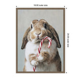Brown and white bunny holding a red and white striped candy cane, shown on a light gray background in a simple brown frame with 18x24 inch outer dimensions.