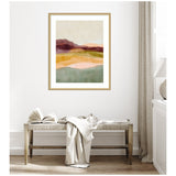 Abstract landscape painting with layered earth tones including green, orange, pink, and purple, framed in light wood, hanging above a rustic bench with white textiles.
