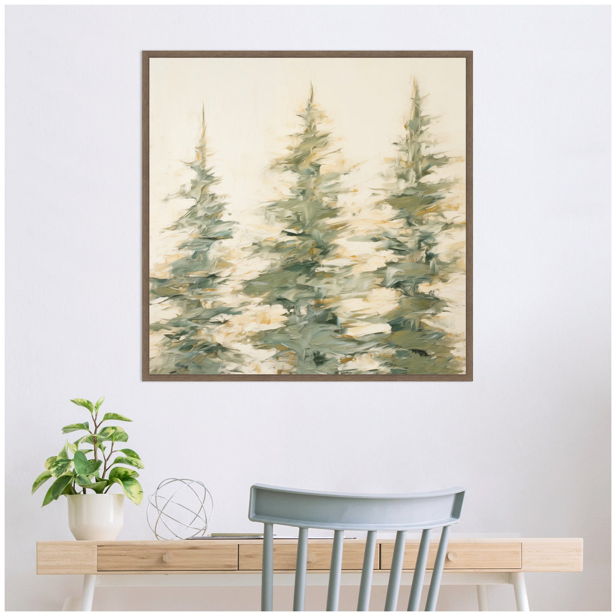 Abstract painting of three evergreen trees with green and beige brushstrokes in a simple brown frame, hung on a white wall above a wooden desk with a plant and decorative object.