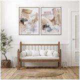 Two abstract canvas paintings in beige, white, gray, and black tones above a wooden bench with white cushions, set against a white wall with a woven round rug below.