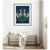 Framed Art Deco style print of two symmetrical herons facing each other with geometric patterns in blue, gold, and beige tones hung above a rustic wooden bench with an open book and draped blanket.