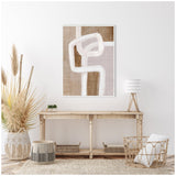 Abstract framed canvas with intertwined rhythmic white lines over beige and taupe textured blocks, hanging above a natural wooden console with woven and wicker decor.