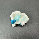 White Stilbite crystal cluster with two translucent blue Cavansite balls embedded, placed on a dark gray surface.
