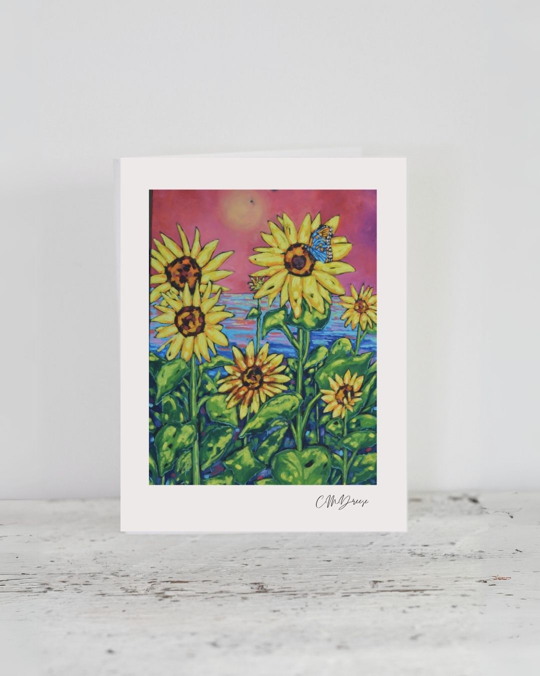 Notecard featuring sunflowers against a rosy sky with a blue butterfly, artwork by Christi Dreese