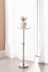 Round white marble top on an adjustable stainless steel pedestal base, holding a small white vase with dried flowers, set near sheer white curtains.