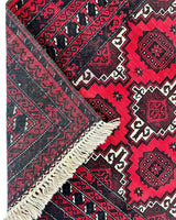 Hand-knotted Afghan Baluch wool rug with deep red, black, and white geometric patterns and intricate borders, featuring one corner flipped to show the backside and natural fringe.