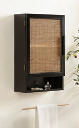 Black wall-mounted cabinet with a rattan woven door panel and open cubby below holding small decorative items, with a towel hanging on a wooden rod beneath.