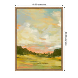 Framed canvas painting of a soft landscape with yellow fields, dark green trees along horizon, and a pastel sky with orange, blue, and white clouds, signed by Annie Quigley.