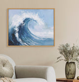 Abstract painterly artwork of a curling ocean wave in shades of blue and white, framed and hung above a beige couch and a green glass vase with dried branches.