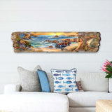 Wooden wall art depicting a retro car parked on a sandy beach with ocean waves, rocky outcrops, and a setting sun in warm tones, mounted above a white sofa.