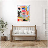 Abstract canvas artwork with colorful shapes and brush strokes in blue, red, black, yellow, and orange, framed and hung on a white wall above a wooden bench with white cushions.